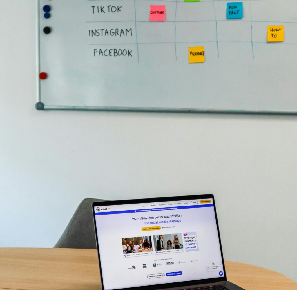 A modern office setup featuring a laptop and a whiteboard schedule for social media platforms.