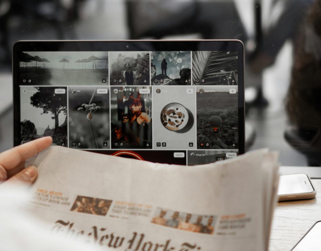 A person reading a newspaper while browsing images on a laptop, symbolizing remote work lifestyle.
