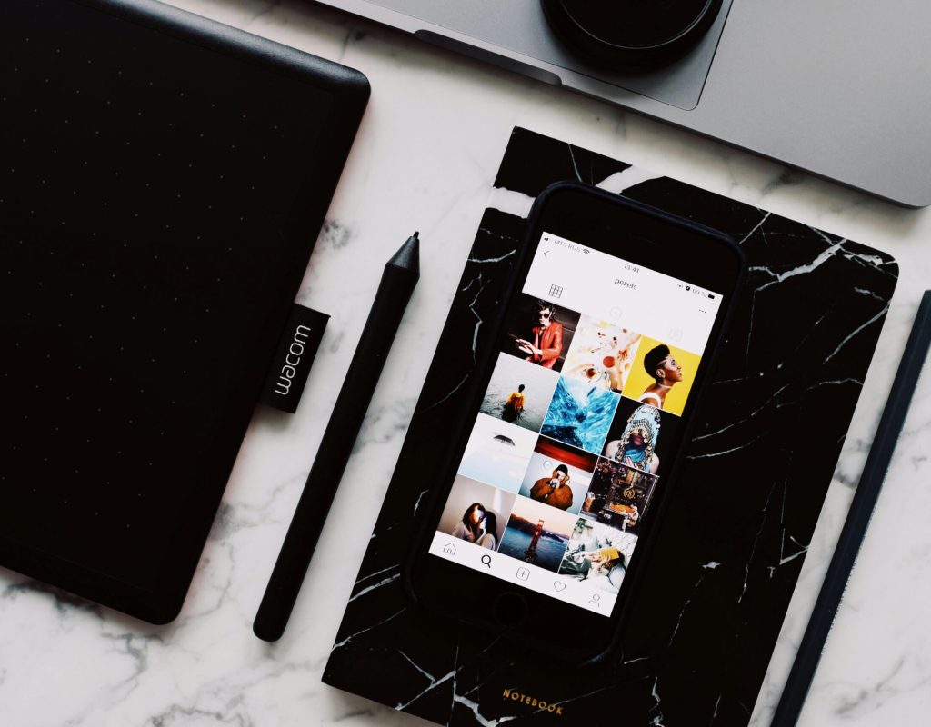 From above of marble table with black textbook and cellphone above with opened app showing interesting photo gallery on screen