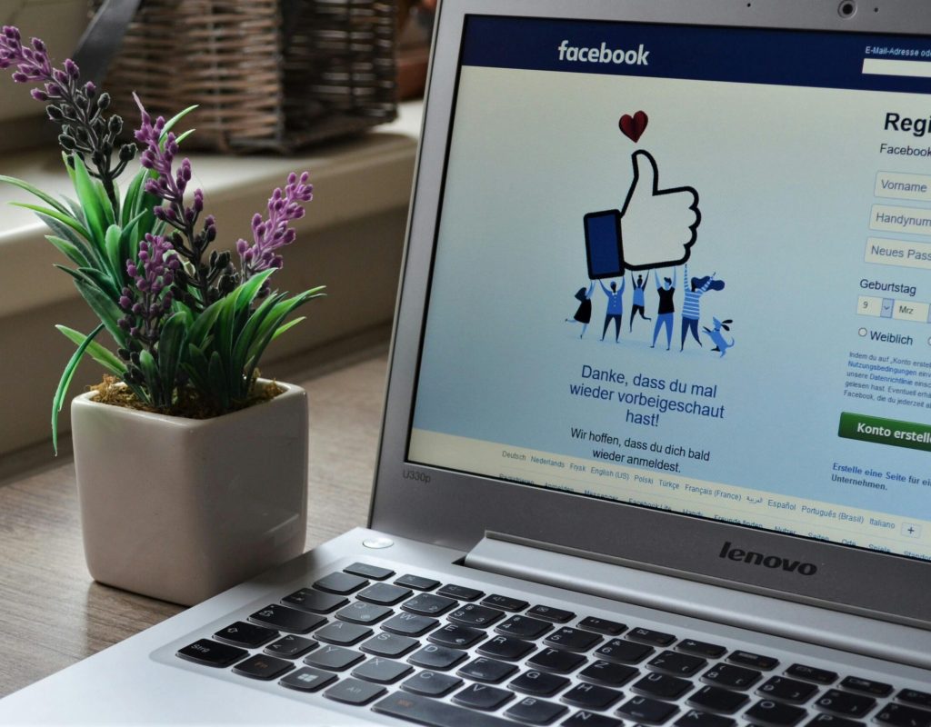 A Lenovo laptop displaying Facebook login beside a lavender plant indoors.